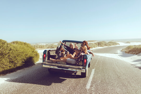 Young and diverse group of people riding in the back of an oldtimer truck on a sandy beach road while on a road trip