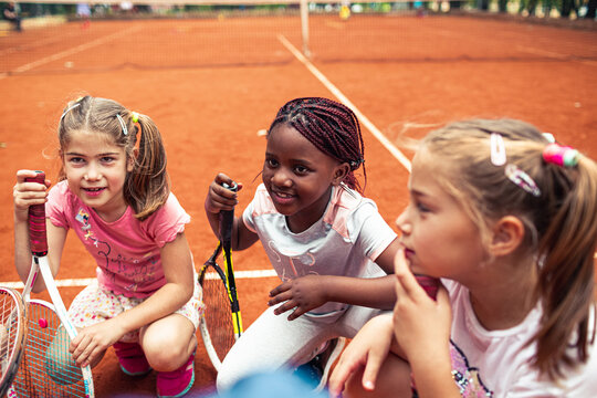 Group of young girls with tennis rackets on clay court smiling