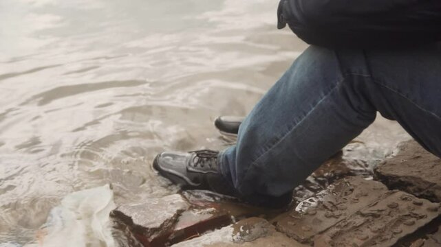 Close-up of feet in shoes of an unemployed, desperate man sitting on a river bank.
