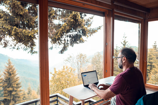 Man working remotely on laptop with mountain view from cabin office