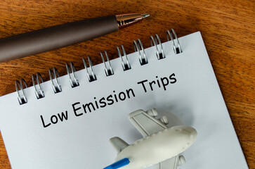 Top view of Low Emission Trips text on white notepad with small airplane and pen background. Environmental awareness