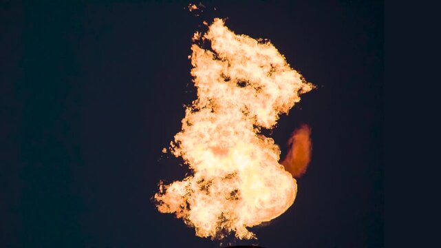 Infernal Flames Blaze in the Dark. A powerful pillar of bright flame with swirling fiery tongues in the air on a black background. Slow Motion