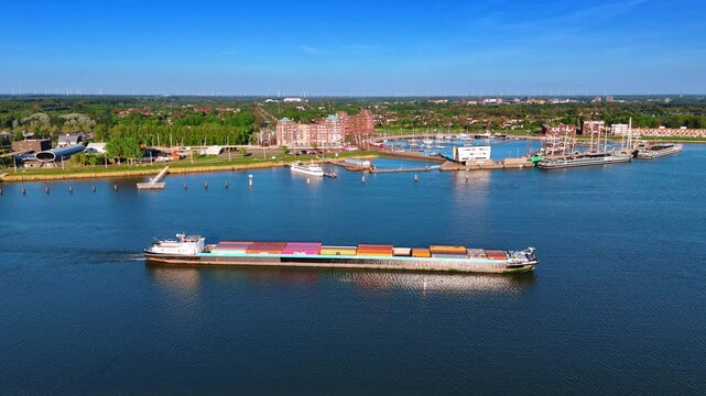 Barge loaded with containers by the beautiful blue waterscape. Port of Lelystad, the Netherlands and green cityscape at backdrop. Aerial view.