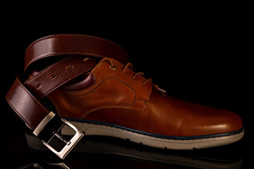 Men's leather belt and shoe on a black background.