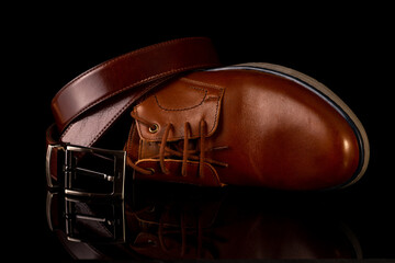 Men's leather belt and shoe on a black background.