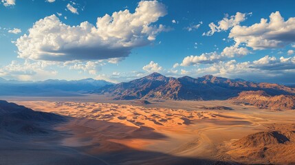 Naklejka premium Vast desert terrain stretches endlessly, showcasing dramatic sand dunes and rugged mountains under a brilliant blue sky dotted with fluffy clouds. The light creates a striking contrast