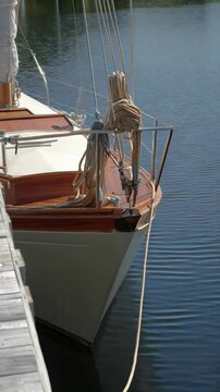 Elegant sailboat moored beside a wooden dock, showcasing the bow, lines, and brightwork details reflecting on calm water.