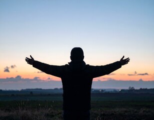Fototapeta premium Silhouette of a person with arms outstretched, enjoying a beautiful sunset over a tranquil landscape.