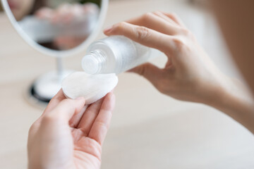 Making beauty routine, attractive asian young woman hand holding cotton pad and bottle, female applying facial wipe on her face remover washing makeup, essence or lotion of skin care treatment at home