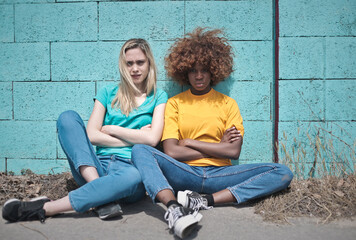 two angry girls sitting leaning against a colored wall