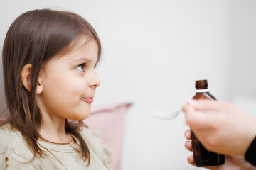 child is sick in bed. Mom gives cough syrup to her daughter. Concept disease, pharmaceutics.