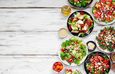 Variety of delicious fresh salads. Overhead view side border on a white wood background. Summer food concept.