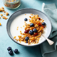 Crunchy Granola with Blueberries in Yogurt Bowl. Blue background. Close up.