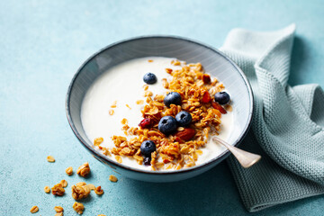 Crunchy Granola with Blueberries in Yogurt Bowl. Blue background. Close up.