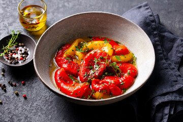 Roasted Peppers in Herb Marinade with Olive Oil in salad bowl. Grey background. Close up.