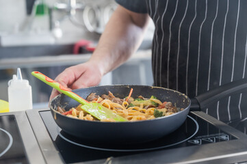 The chef cooks pasta in a frying pan. 