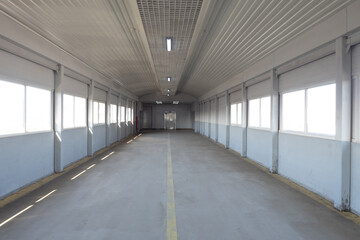 Long corridor with concrete floor. Path to elevator inside building. Corridor with windows on...