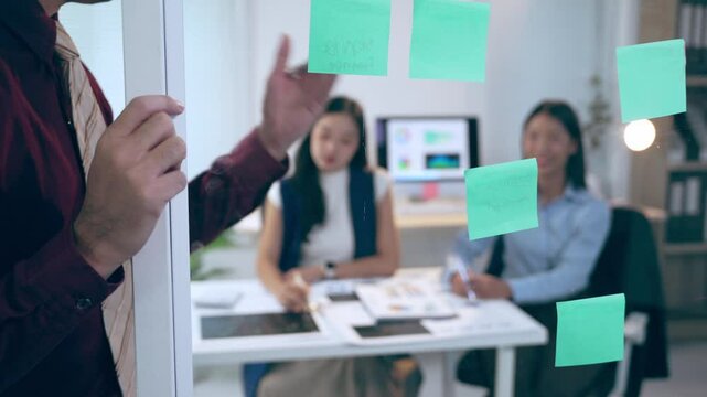 Business team brainstorming and discussing new ideas using sticky notes on a glass wall in a modern office