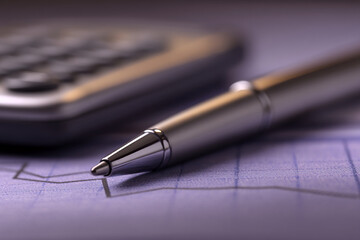 Fototapeta premium Close-up of silver pen on purple graph, blurred calculator background. Represents business, finance, analysis, precision