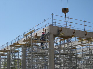 Reinforced concrete building under construction with a crane hook against a blue sky background -...