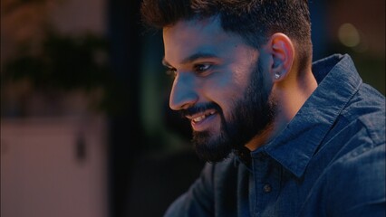 Overtime night working Indian businessman male guy manager business man at dark evening office working with laptop computer browsing at desk smiling employer worker programming online commerce project