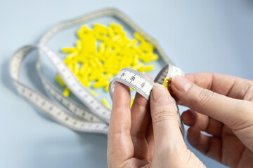 Female hands holding a measuring tape against pile of yellow pills
