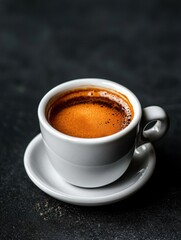 Fototapeta premium Close-up of a white coffee cup and saucer on a black textured surface. the cup is filled with a dark brown liquid, which appears to be freshly brewed coffee.