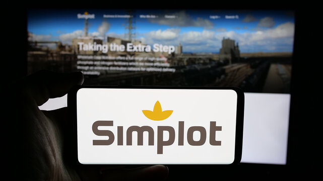 Stuttgart, Germany - 04-26-2025: Person holding cellphone with logo of US agribusiness J. R. Simplot Company on screen in front of webpage. Focus on phone display.
