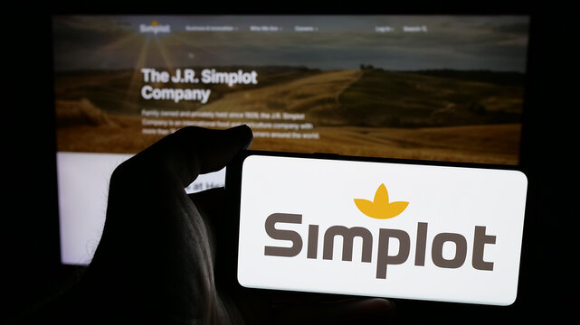 Stuttgart, Germany - 04-26-2025: Person holding mobile phone with logo of US agribusiness J. R. Simplot Company on screen in front of web page. Focus on phone display.