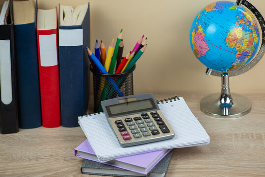 On a study desk, you will find a calculator, various notebooks, and a globe placed neatly