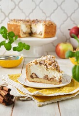 Sliced ​​round pie on shortcrust pastry with apples, walnuts and sour cream soufflé on white plate on light wooden background. Recipes apples.