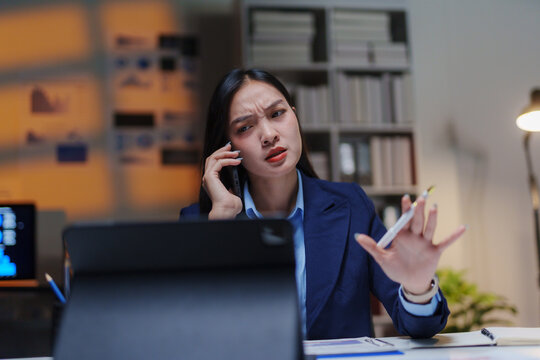 Young Asian businesswoman arguing on the phone while working late in the office, feeling overwhelmed by deadlines and pressure