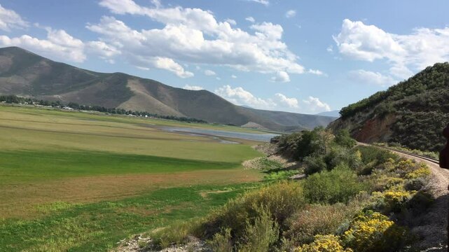 Looking out of the window of an old train in Heber Utah at Heber Valley, Deer Creek Reservoir in the background. Bright green grass in the valley.  Handheld camera from a train.