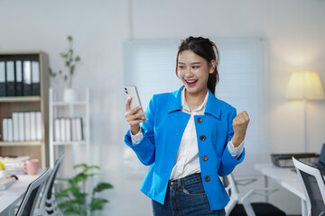 Excited businesswoman celebrating success while holding a smartphone in a bright, modern office,...