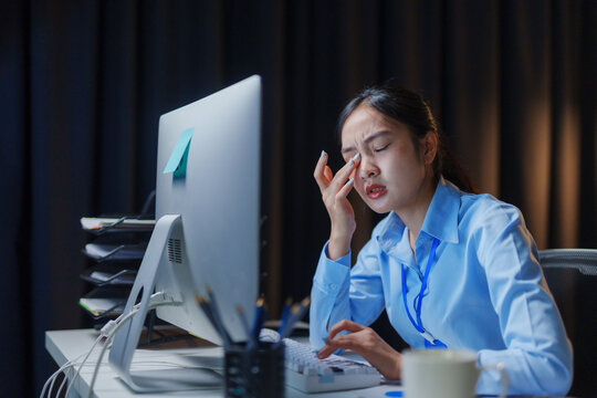 Young professional experiencing eye strain from prolonged computer use in a dimly lit office, highlighting the challenges of modern work life - Powered by Adobe
