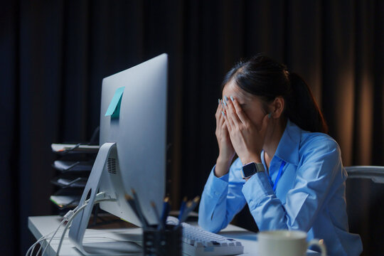 Exhausted office worker battling burnout and frustration while laboring late into the night, surrounded by the glow of screens and paperwork