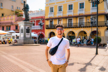 Happy young Latino tourist with glasses, white t-shirt and khaki pants smiling in Cartagena's...