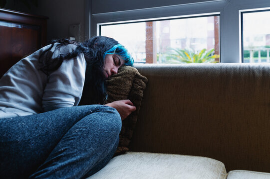 Sad woman with blue hair suffering from depression, lying on sofa at home