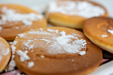 Brown pancakes with emoji smiley faces sprinkled with powdered sugar located on a white plate. All the pancakes are round.