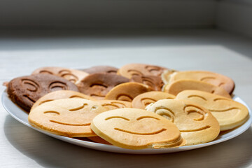 Plate of emoji face pancakes in various shades, playful breakfast concept on a light wooden surface.