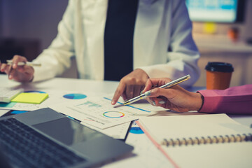 Business team discussing and analyzing financial charts and graphs using pen and laptop at office desk
