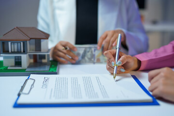 Client signing a contract to buy a house and receiving the keys from a real estate agent, with money and a miniature house on the table