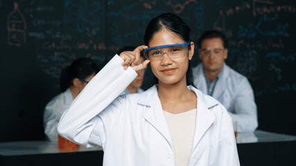 Highschool girl looking at camera while people doing experiment at laboratory. Young cute student...