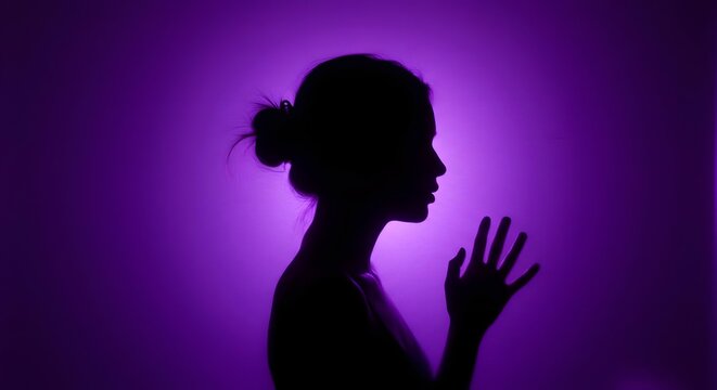 Silhouette of a woman with her hand extended, bathed in a soft purple light from behind. Violence against women. Femicide.