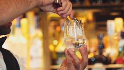 Closeup smart bartender putting ice cube with pouring soda or tonic into glass to serve customer at...