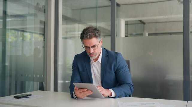 Executive man in suit working using computer for financial business banking work. Focused senior mature Indian or Latin entrepreneur businessman looking at digital tablet screen in office. Copy space 