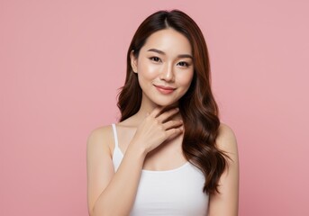 Fototapeta premium Beautiful young woman with smooth skin and long brown hair posing against a pink background in a white