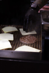 chef poniendo queso sobre la carne de hamburguesas que se están friendo en la parilla