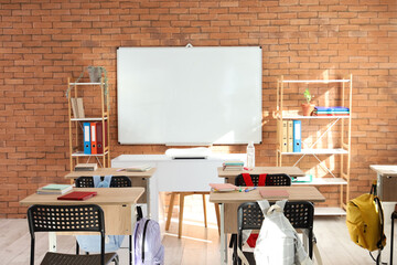Interior of empty classroom with whiteboard, desks and shelf units