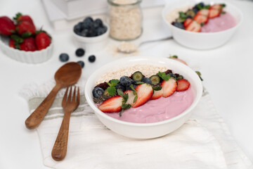 Presented by fruits putting yogurt toppings with strawberry, berry, oats, raisins and chia seed decorated by peppermint in white blow. Pink background. Set of healthy dairy product choice. Pecuniary.